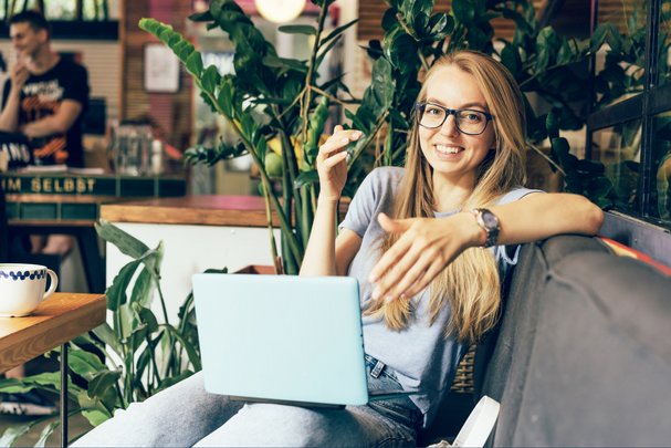 Eine junge Frau sitzt auf dem Sofa mit dem Laptop auf dem Schoß und berät jemanden