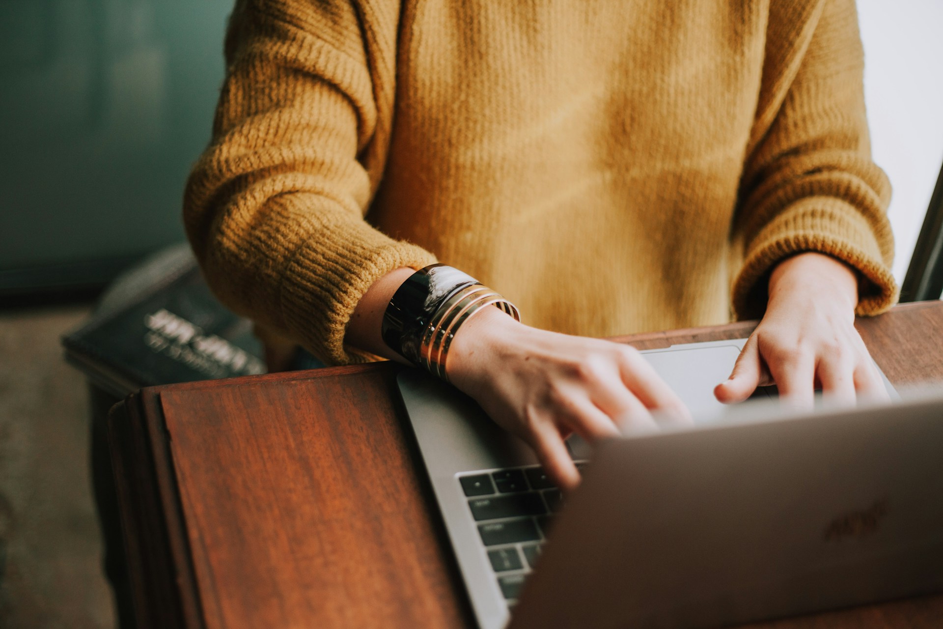 Frau in einem gelben Pullover sitzt vor ihrem Laptop und tippt auf der Tastatur